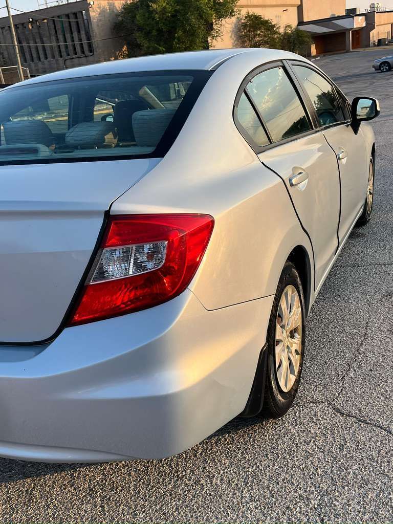 Silver sedan parked on a gravel driveway near a house, rear side view.
