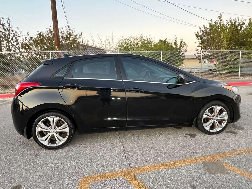 Black hatchback car parked on a street at sunset, side view with chain-link fence in background