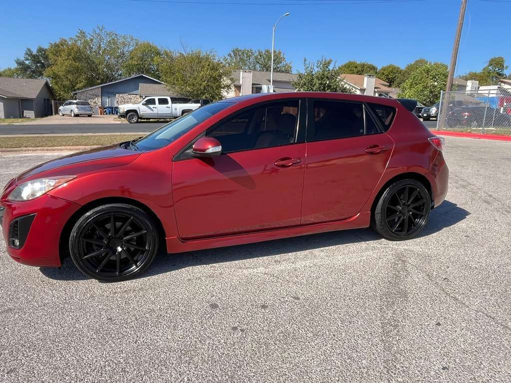 Red hatchback parked on a gravel lot under a clear sky.