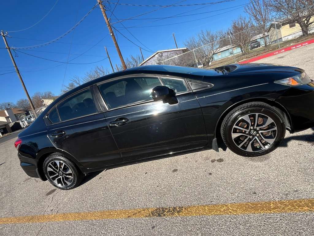 Black sedan parked on a sunny street, side view with power lines overhead.