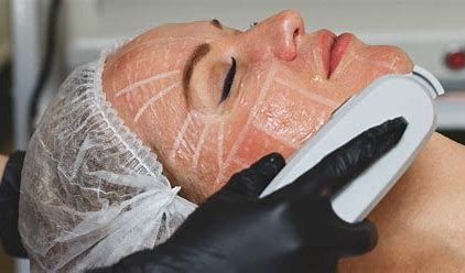 Facial treatment in progress with a woman lying down, wearing a white hair cap and receiving a device on her chin