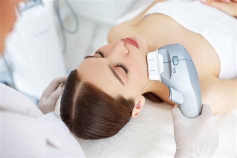 Woman receiving neck massage with handheld device while lying on a white treatment bed