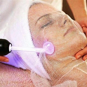Person receiving facial light therapy with a purple glow under a mesh mask