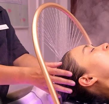 Person receiving a scalp massage with a circular head frame in a pink-lit spa setting
