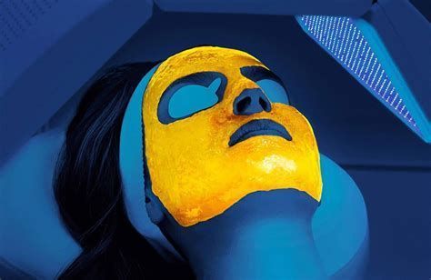Person wearing a yellow face mask under blue UV light, reclining with eyes closed.