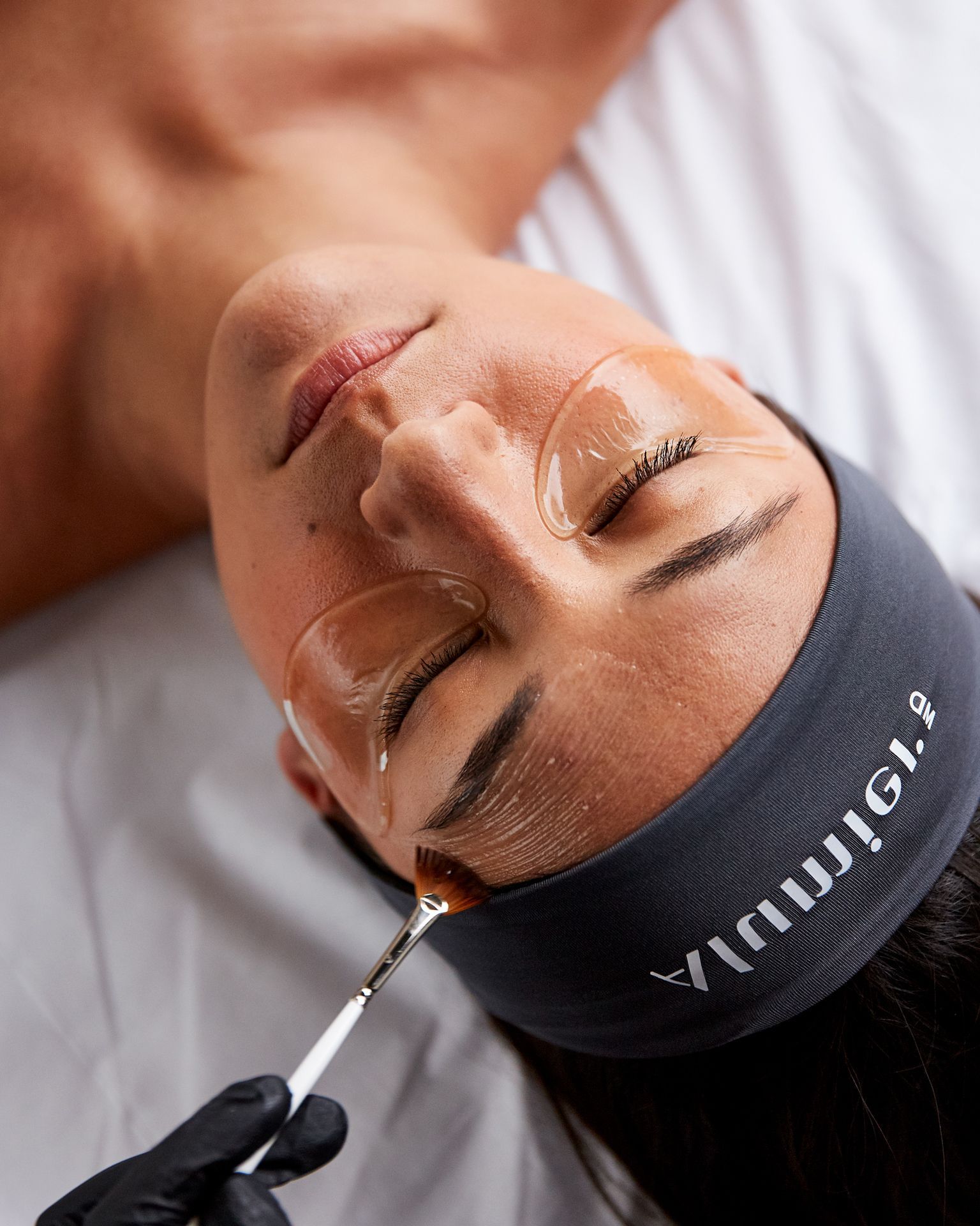 Cosmetologist applying eyebrow treatment with a fine brush to a woman's closed eye and brow area