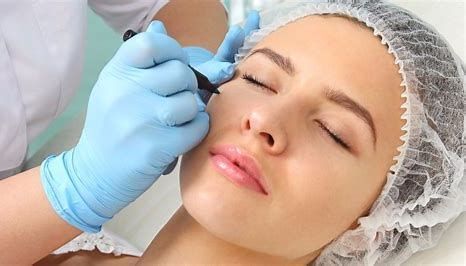 Gloved hand applying eyebrow treatment to a woman lying down with a hairnet on her head