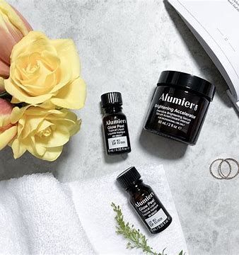 Skincare jars and bottles on a light gray surface with yellow flowers and small rings