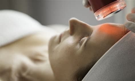 Close-up of a facial treatment with a glowing red light device near a relaxed person's face