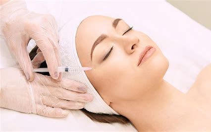 Gloved hand gives facial injection to a reclining patient in a spa-like setting