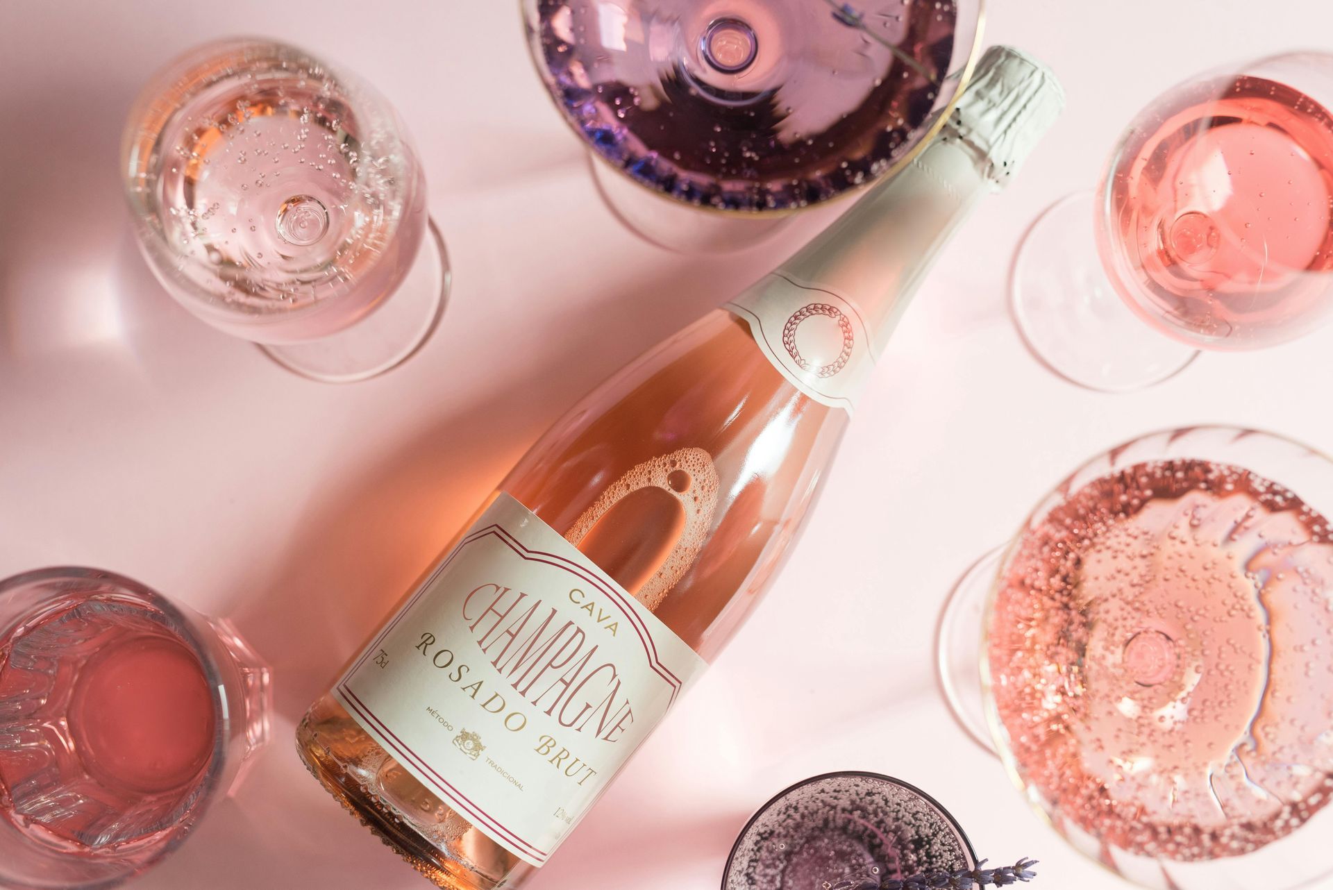 Rosé wine bottle surrounded by pink and purple wine glasses on a pale pink background
