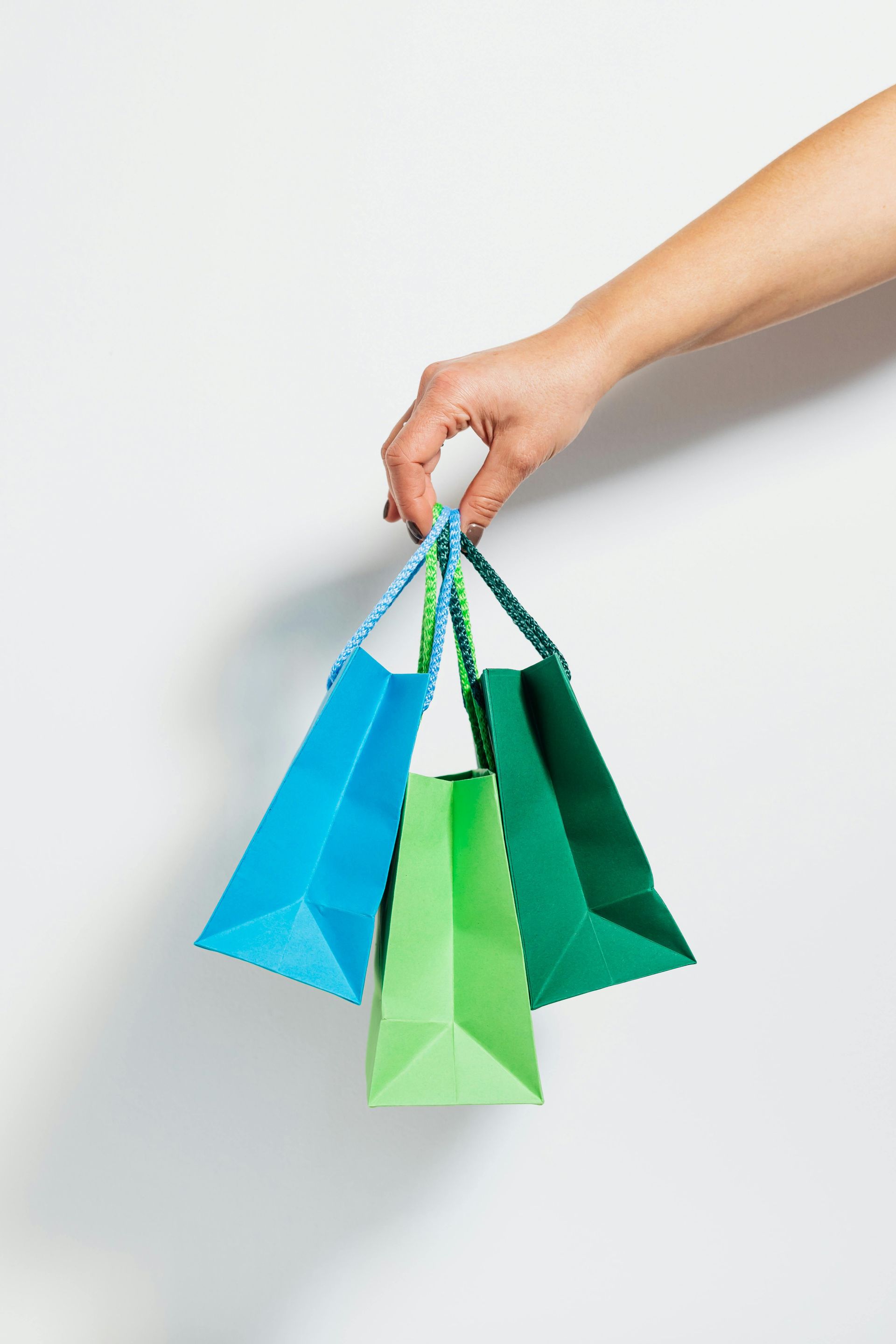 Hand holding three colorful shopping bags: blue, green, and teal.