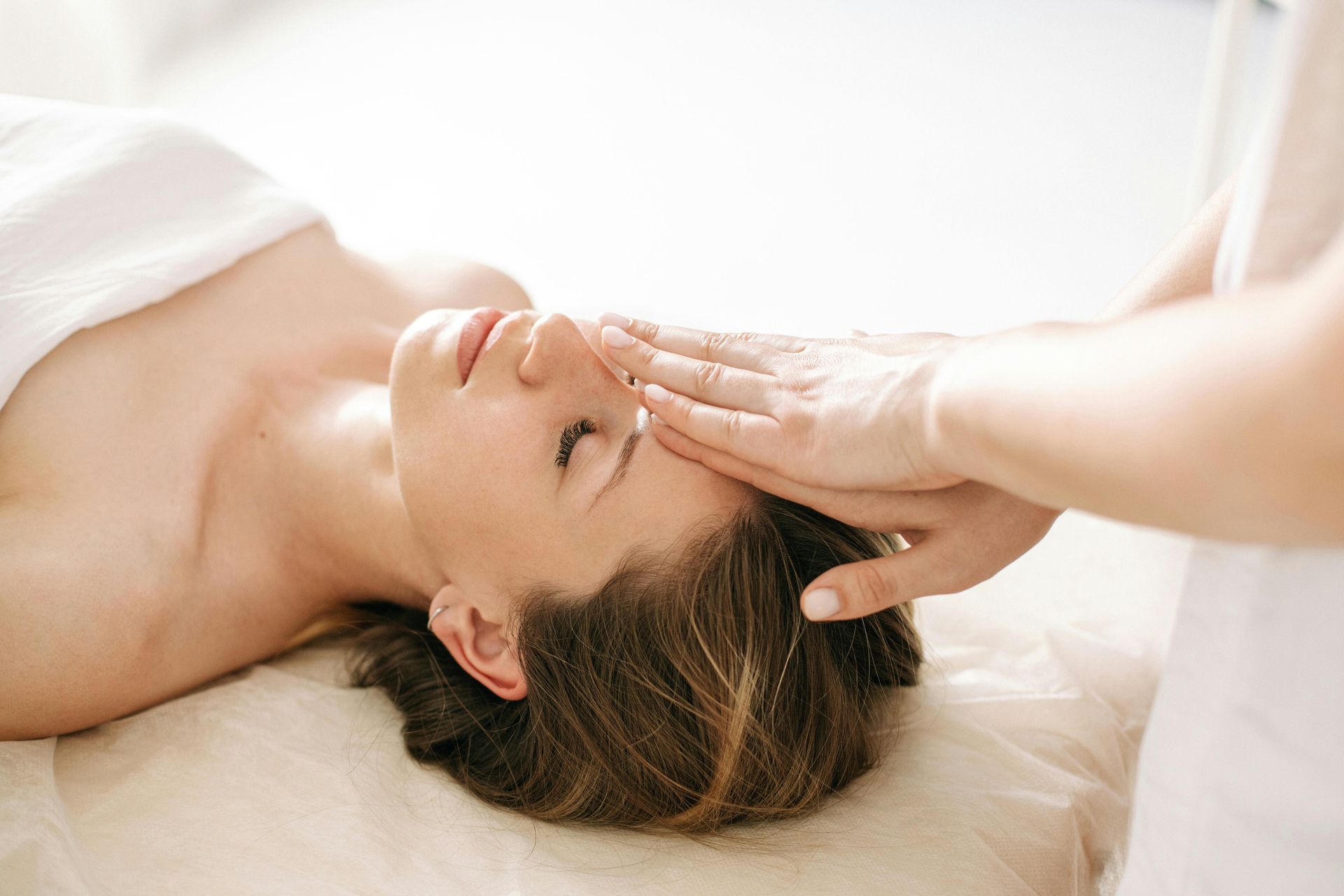 Woman receiving a head massage while lying on a spa table, eyes closed in relaxation.