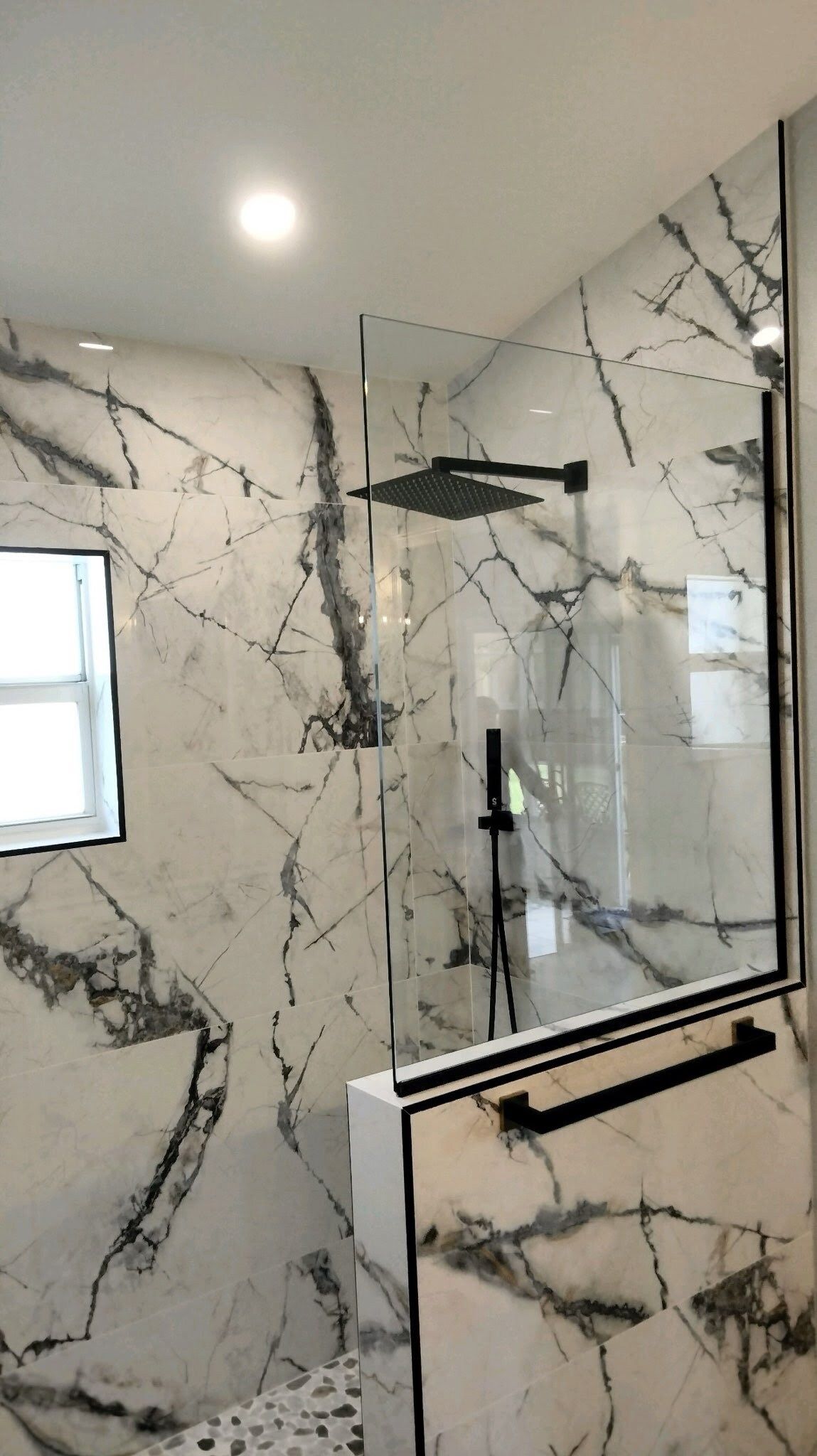 A bathroom with marble walls and a walk in shower with a glass door.