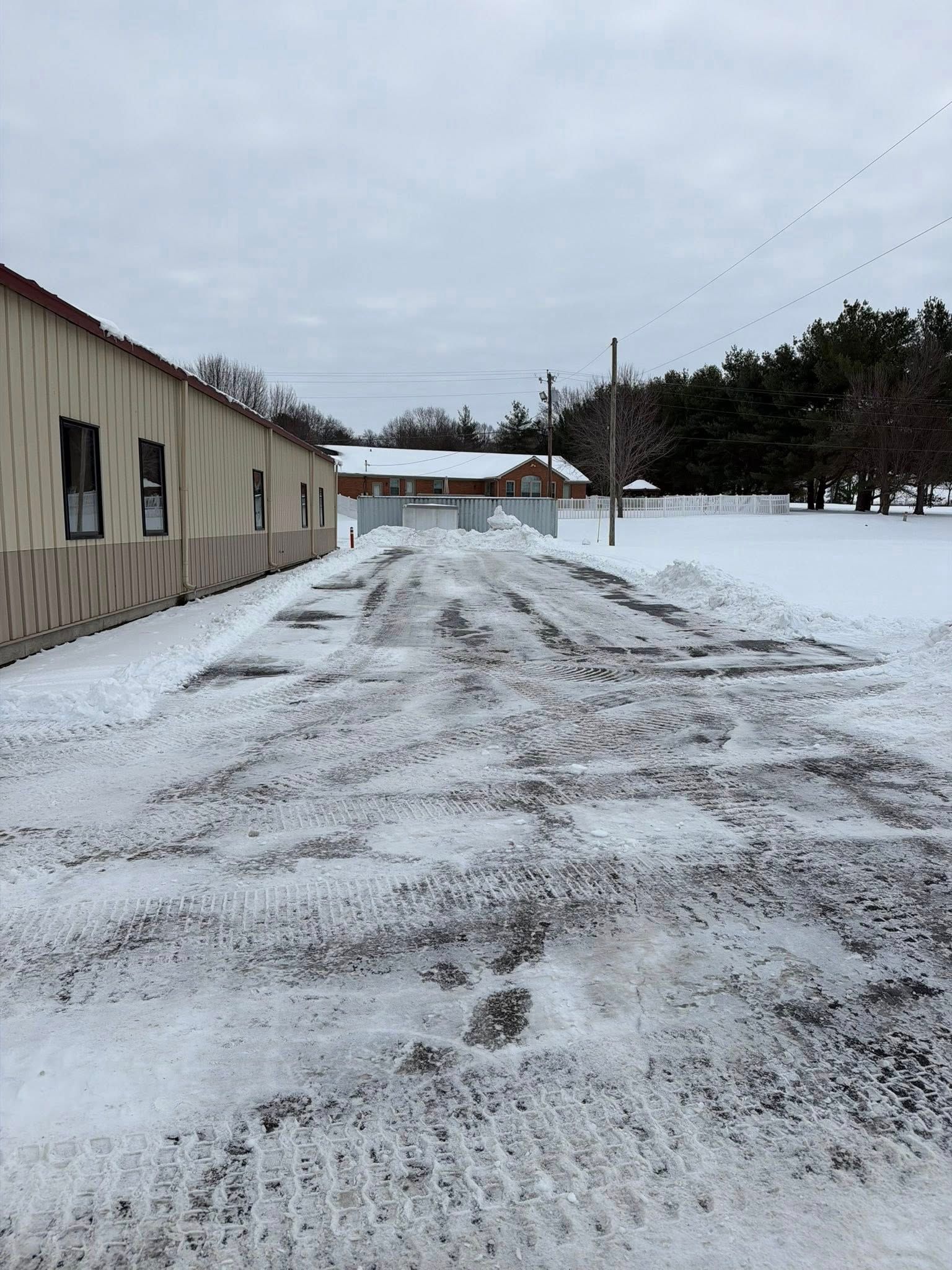 Snow-covered driveway beside a beige building under a cloudy winter sky