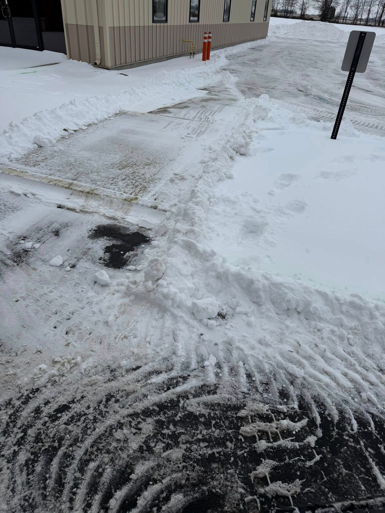 Snow-covered sidewalk and driveway beside a building, with footprints and a red fire hydrant in the distance.