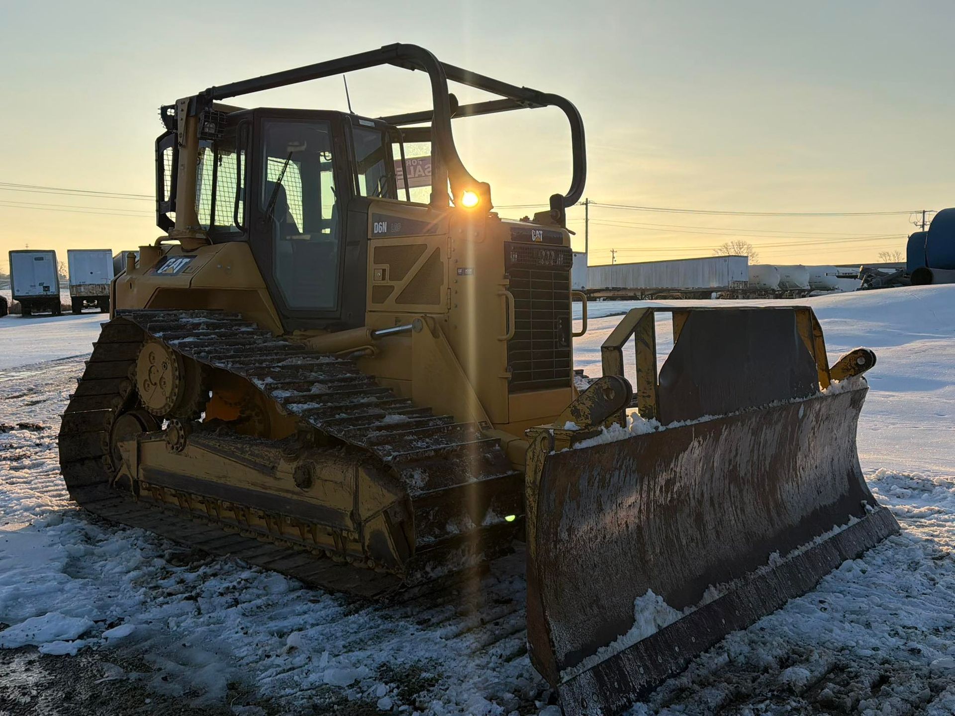 Yellow bulldozer with front blade parked on snowy ground at sunset