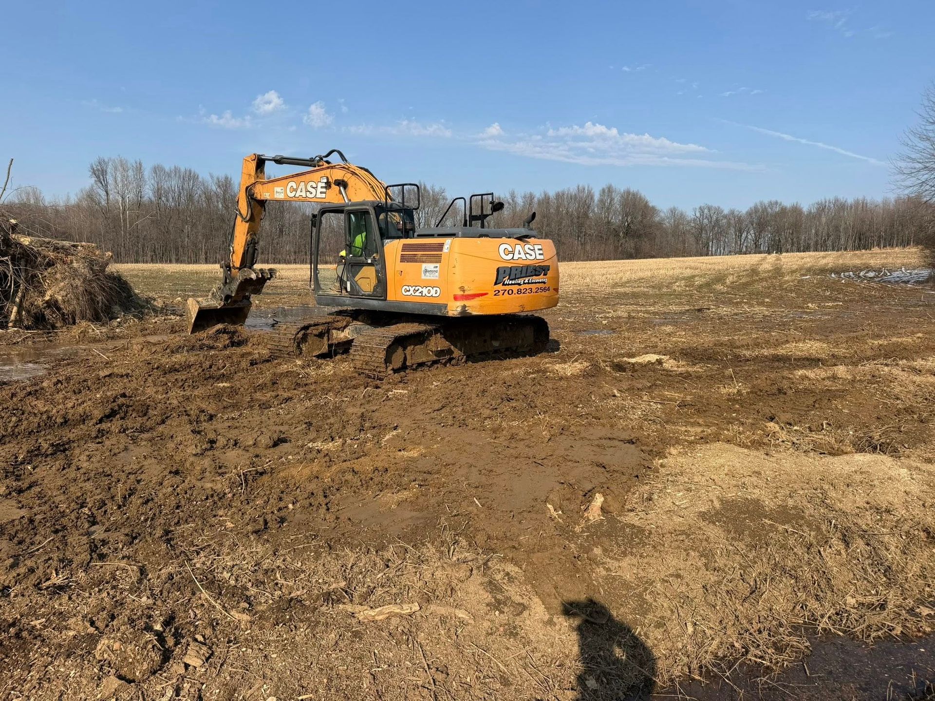 Orange excavator digging in a muddy field under a clear blue sky