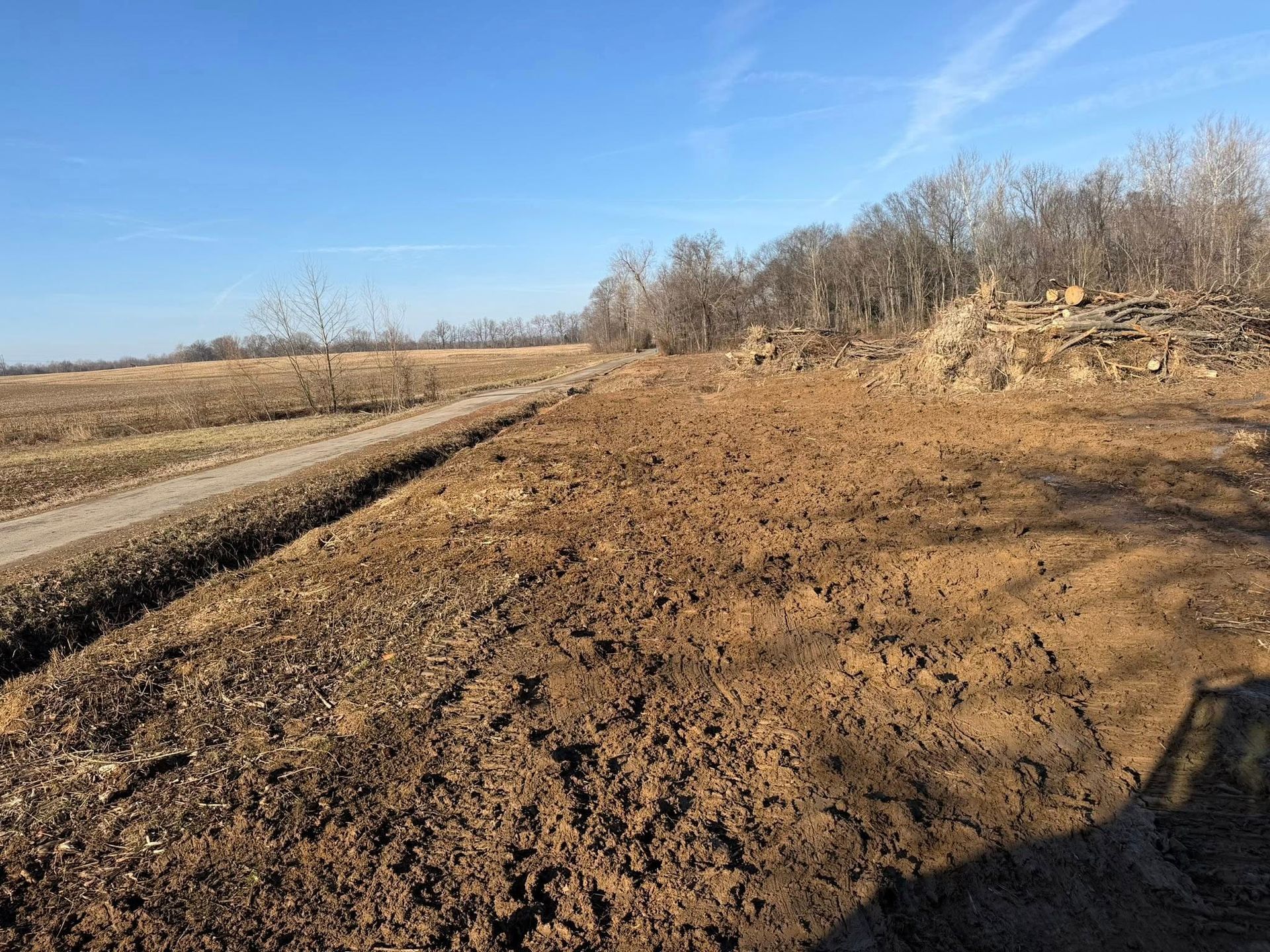 Freshly dug dirt path beside a plowed field under a clear blue sky