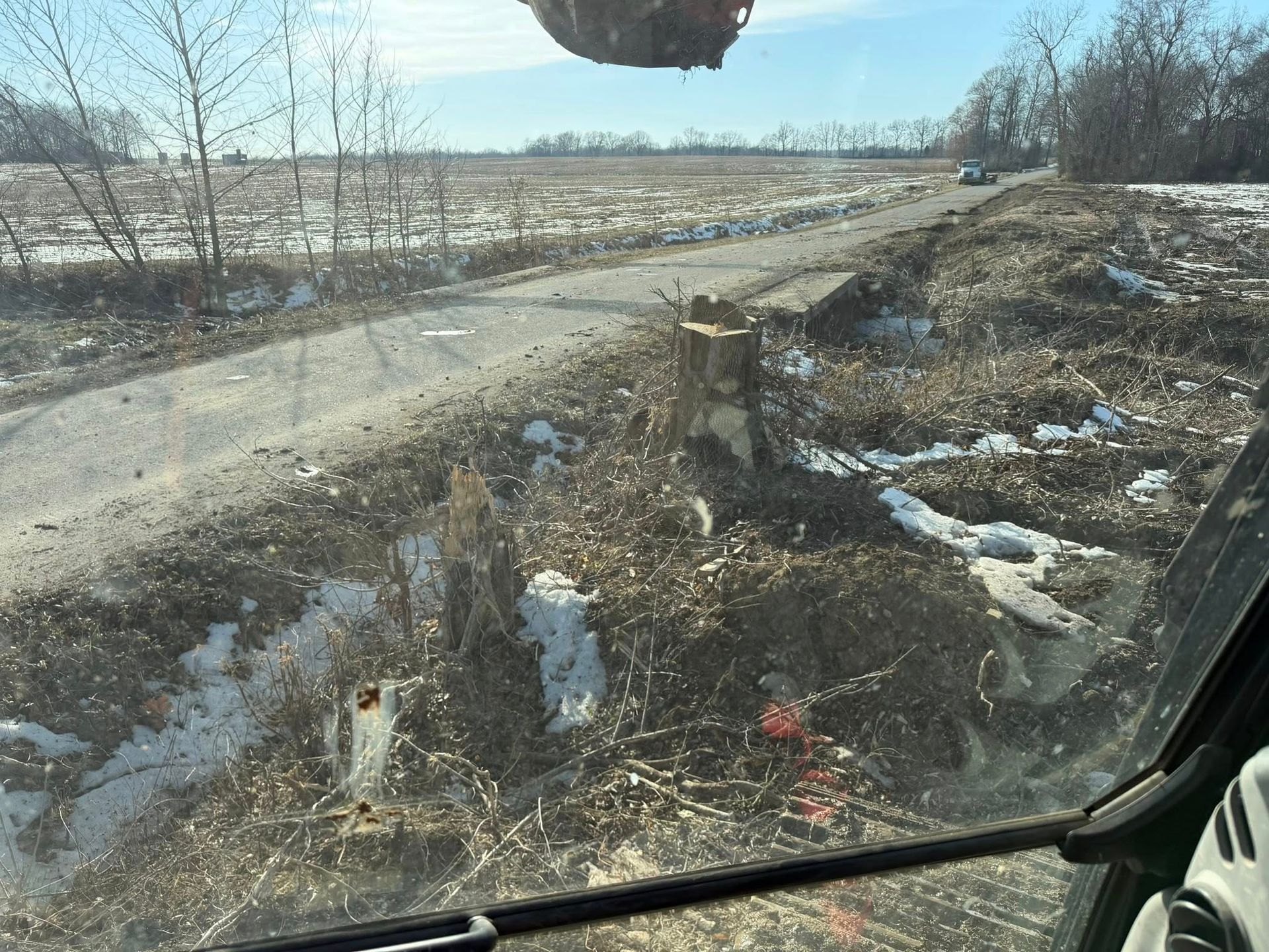 Dirt road beside a muddy ditch with scattered litter and patches of snow under a cloudy sky
