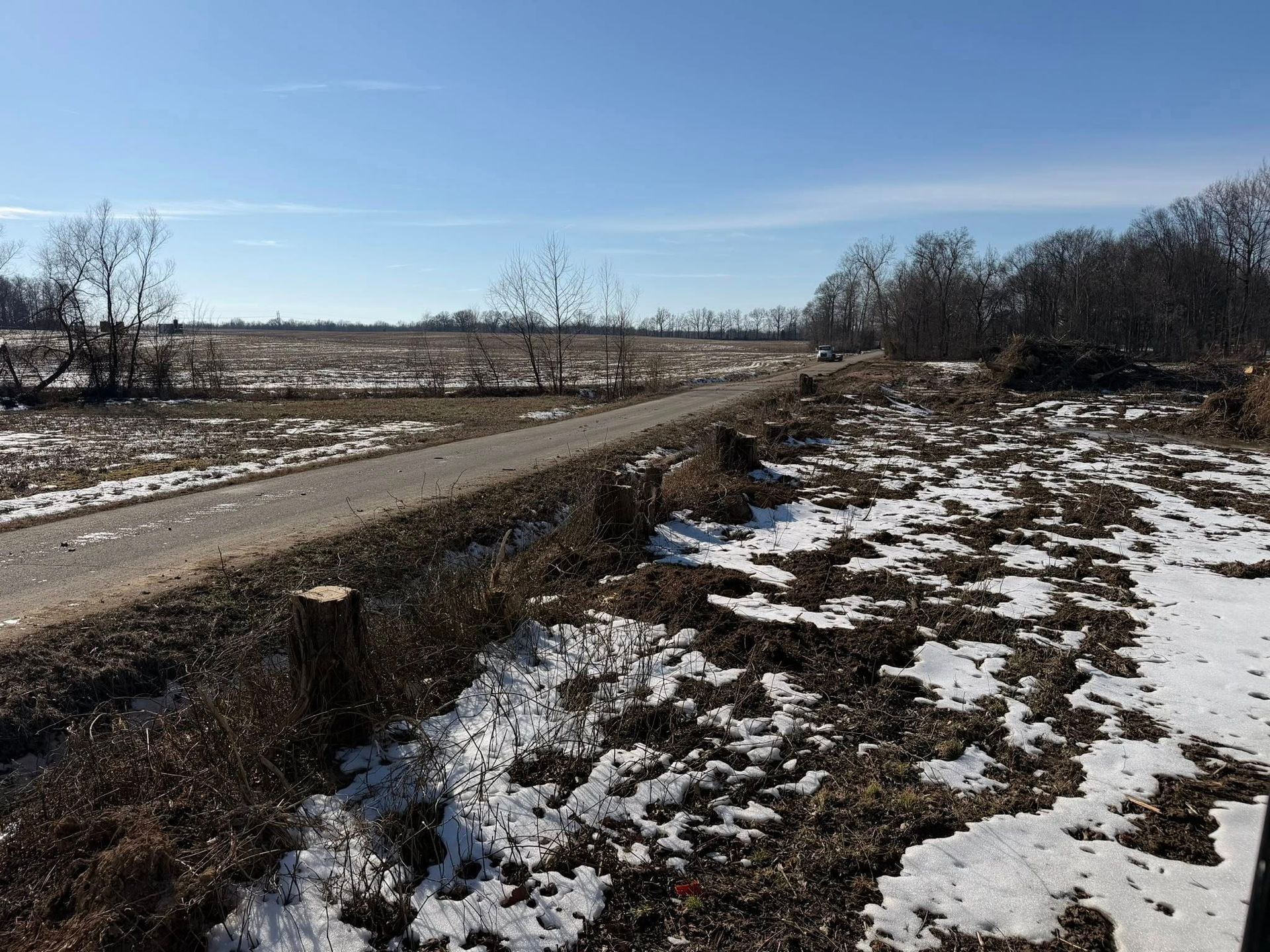 Snowy rural roadside beside a dirt road under a clear blue sky