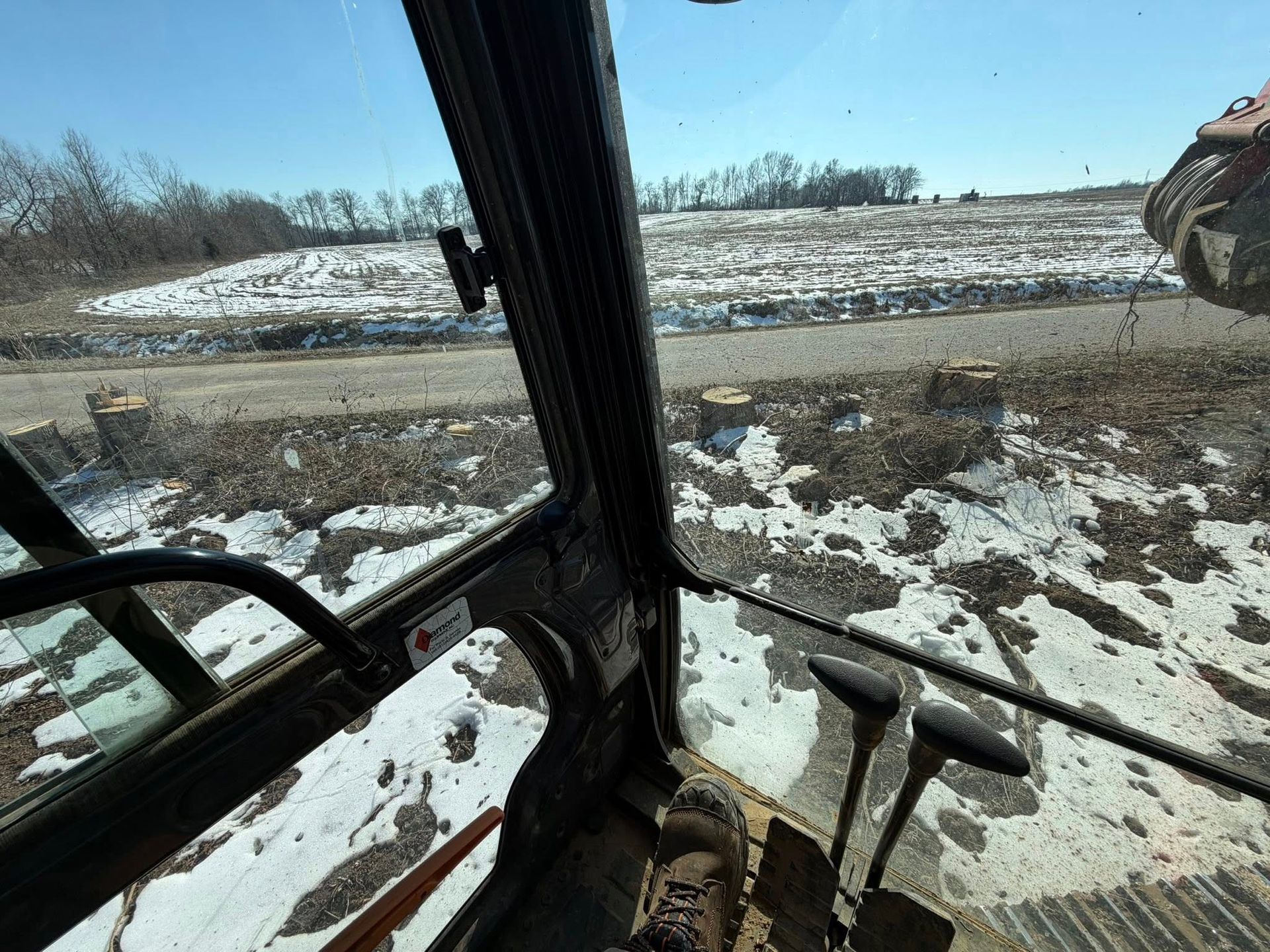 Inside a vehicle cab, looking out at a snowy roadside and a construction vehicle on the right.