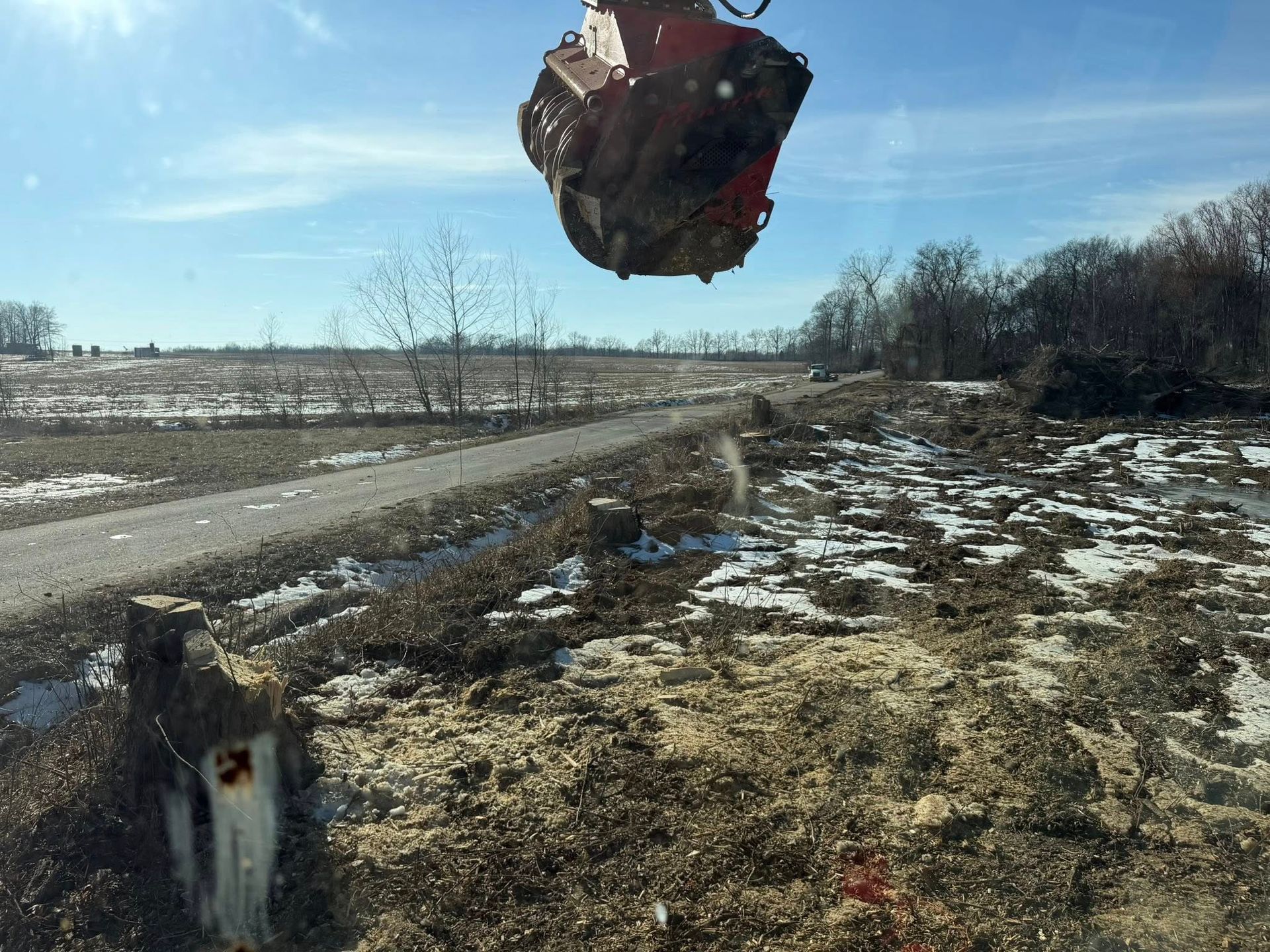 Large red vehicle flipped in the air over a muddy rural road with snow patches.