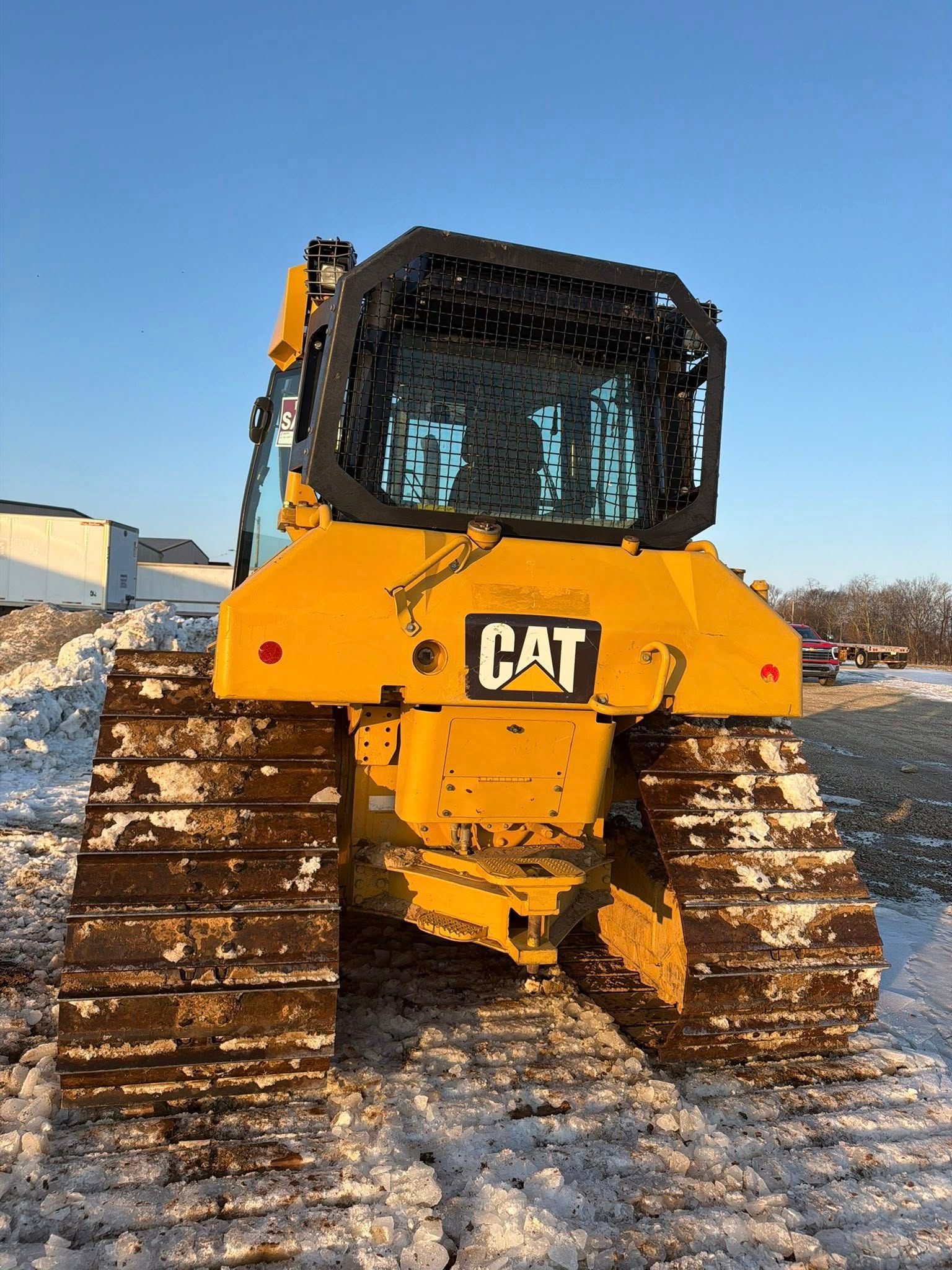 Yellow CAT bulldozer with metal tracks on snowy ground under a blue sky