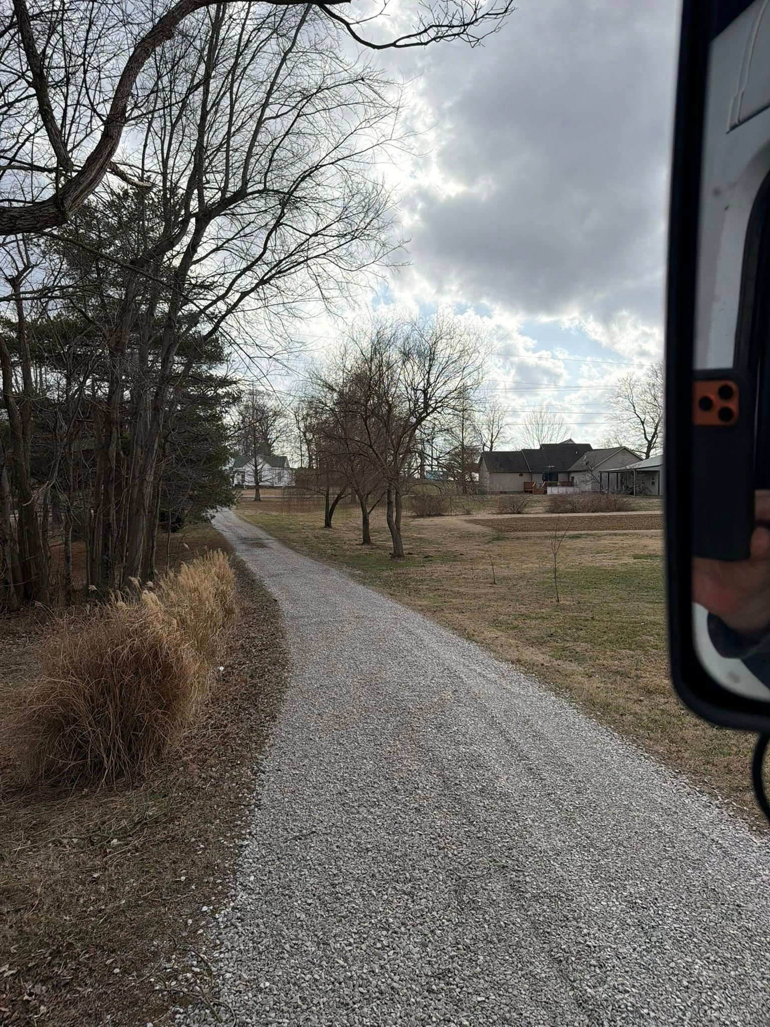 Gravel path curving through a grassy field, with bare trees and cloudy sky on a winter day.