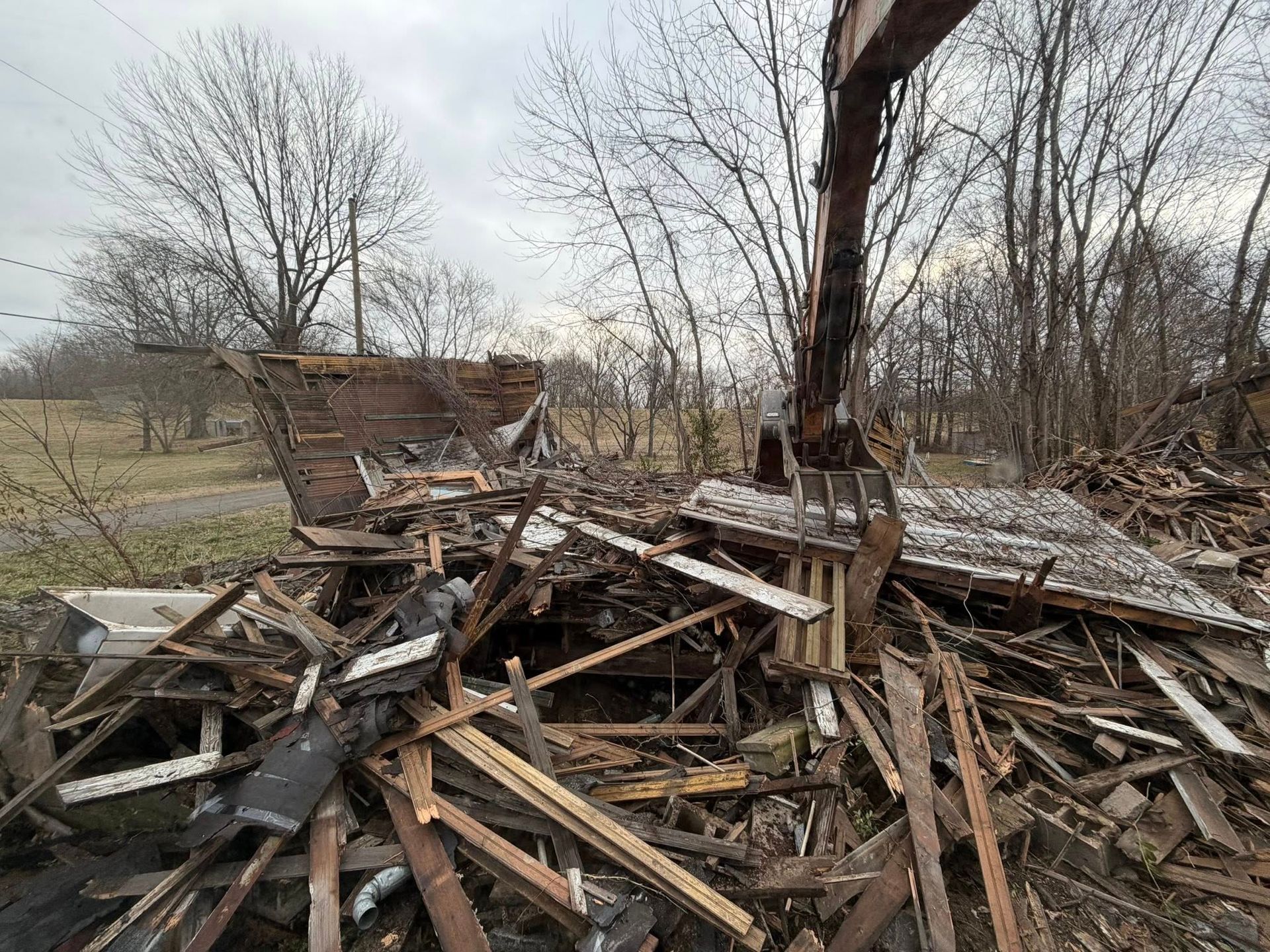 Collapsed wooden structure in a bare field, with a tree and scattered debris in the foreground.