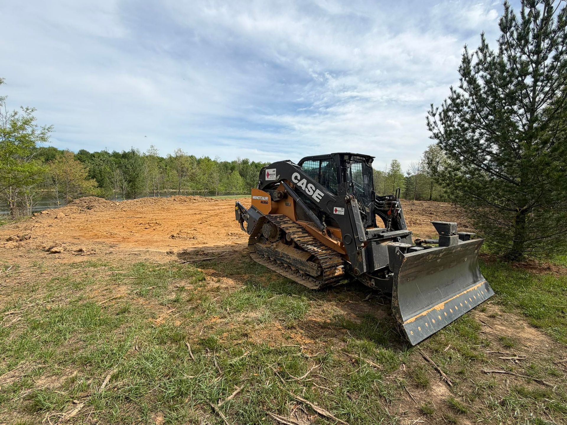 Skid steer bulldozer clearing dirt on a grassy field under a cloudy sky