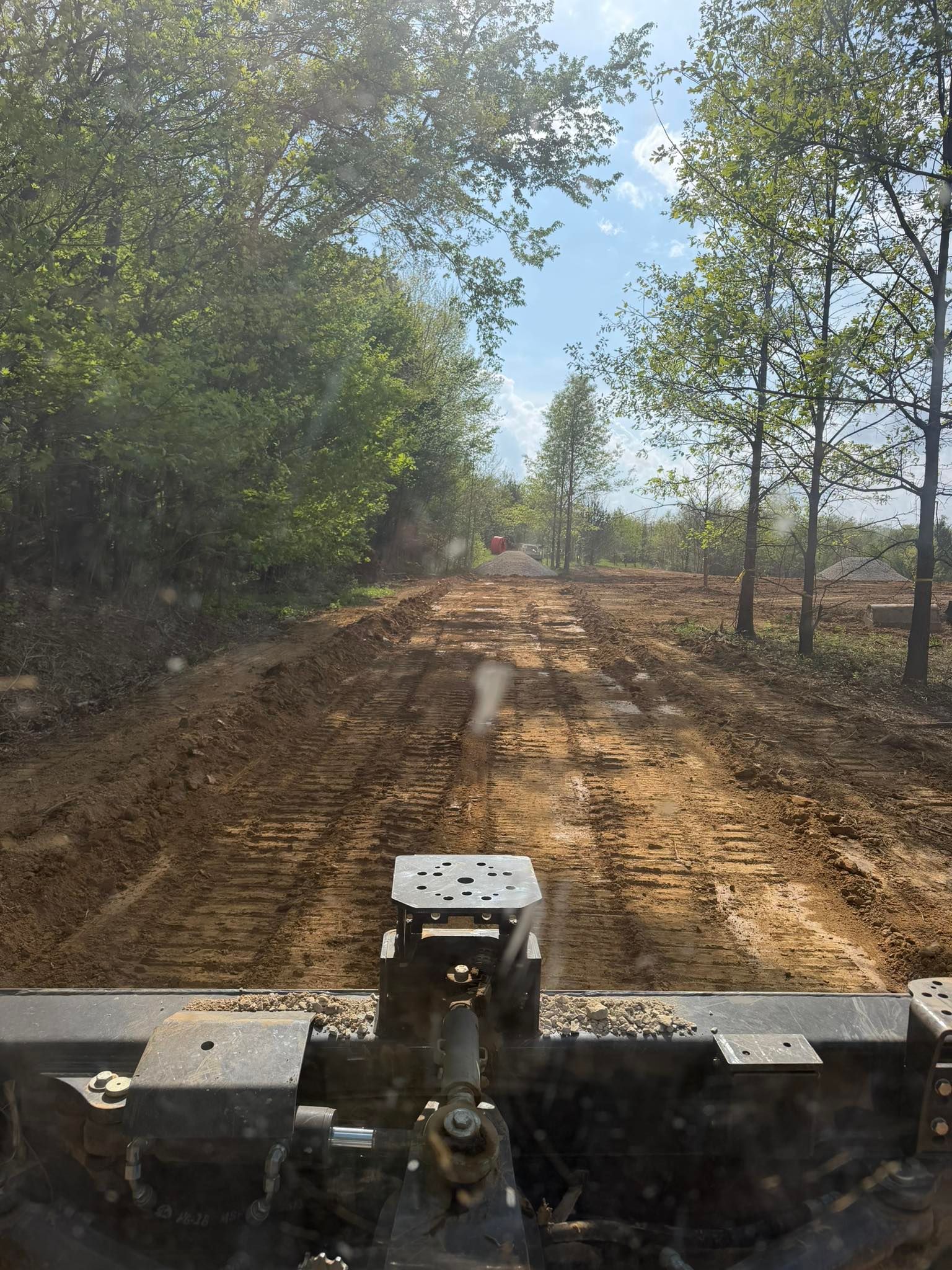 View from a vehicle on a muddy dirt road through trees under a clear blue sky