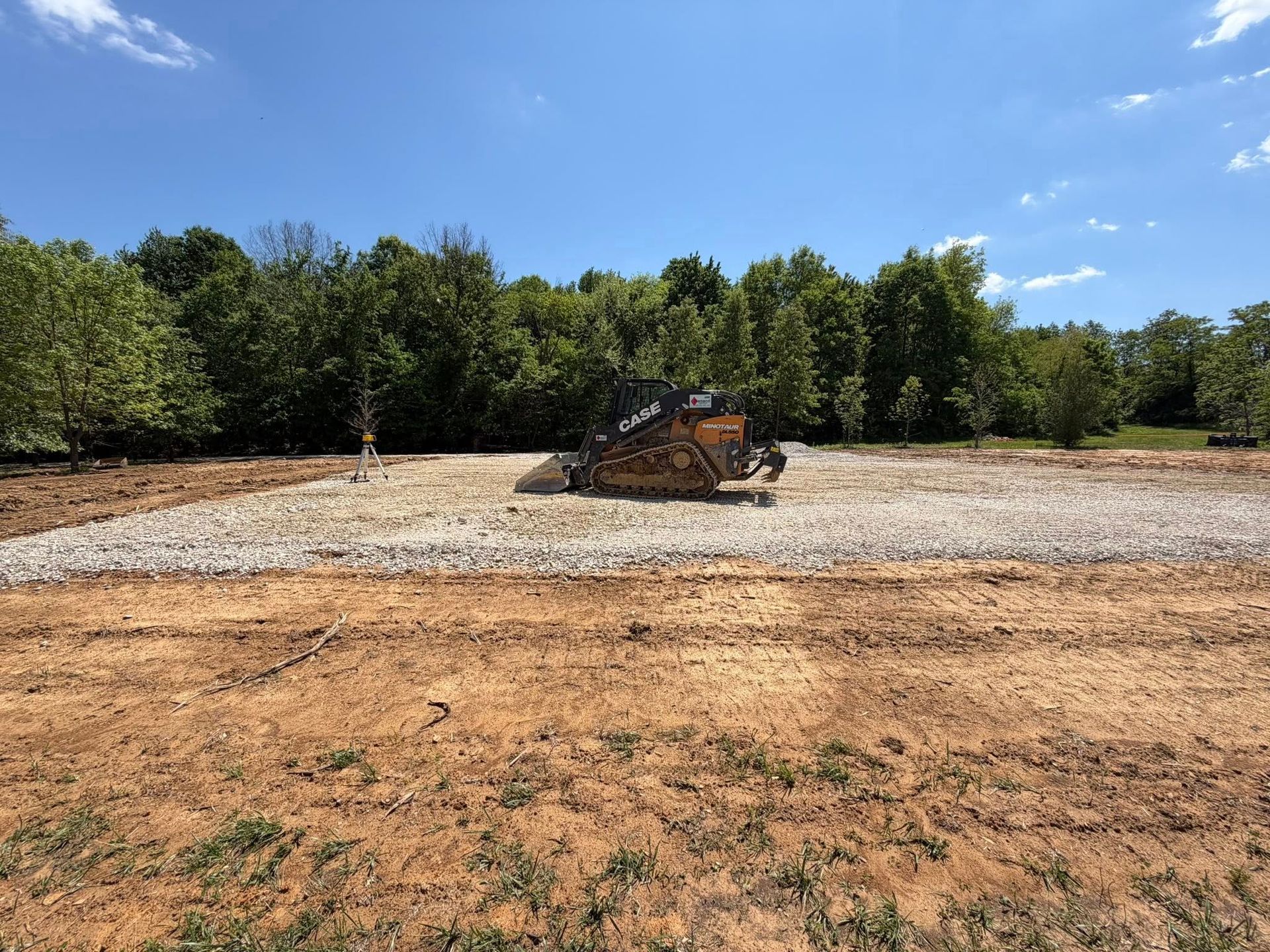 Bulldozer on a gravel lot beside dirt and trees under a blue sky