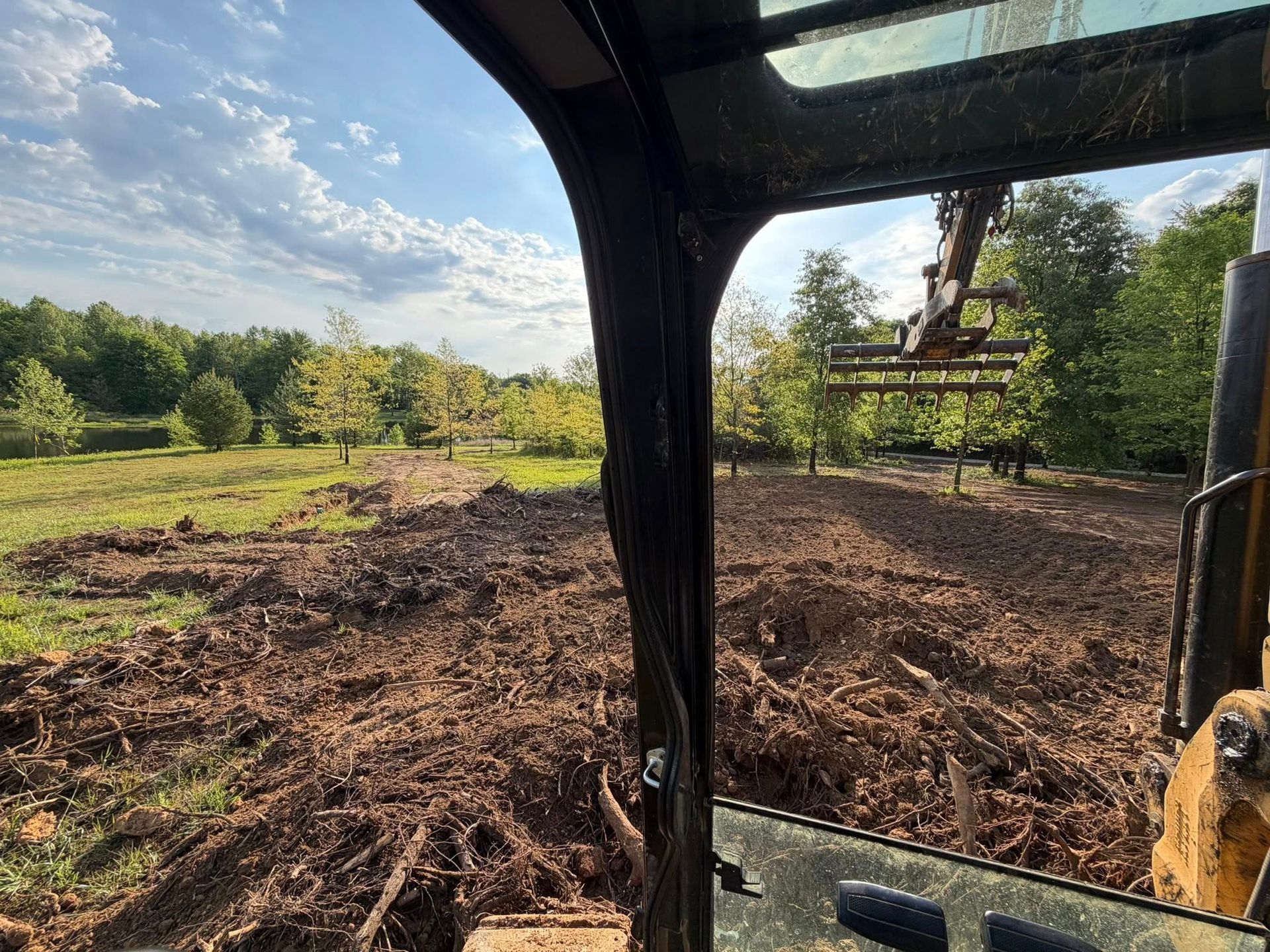View from a tractor cab over a freshly cleared field with trees and blue sky.
