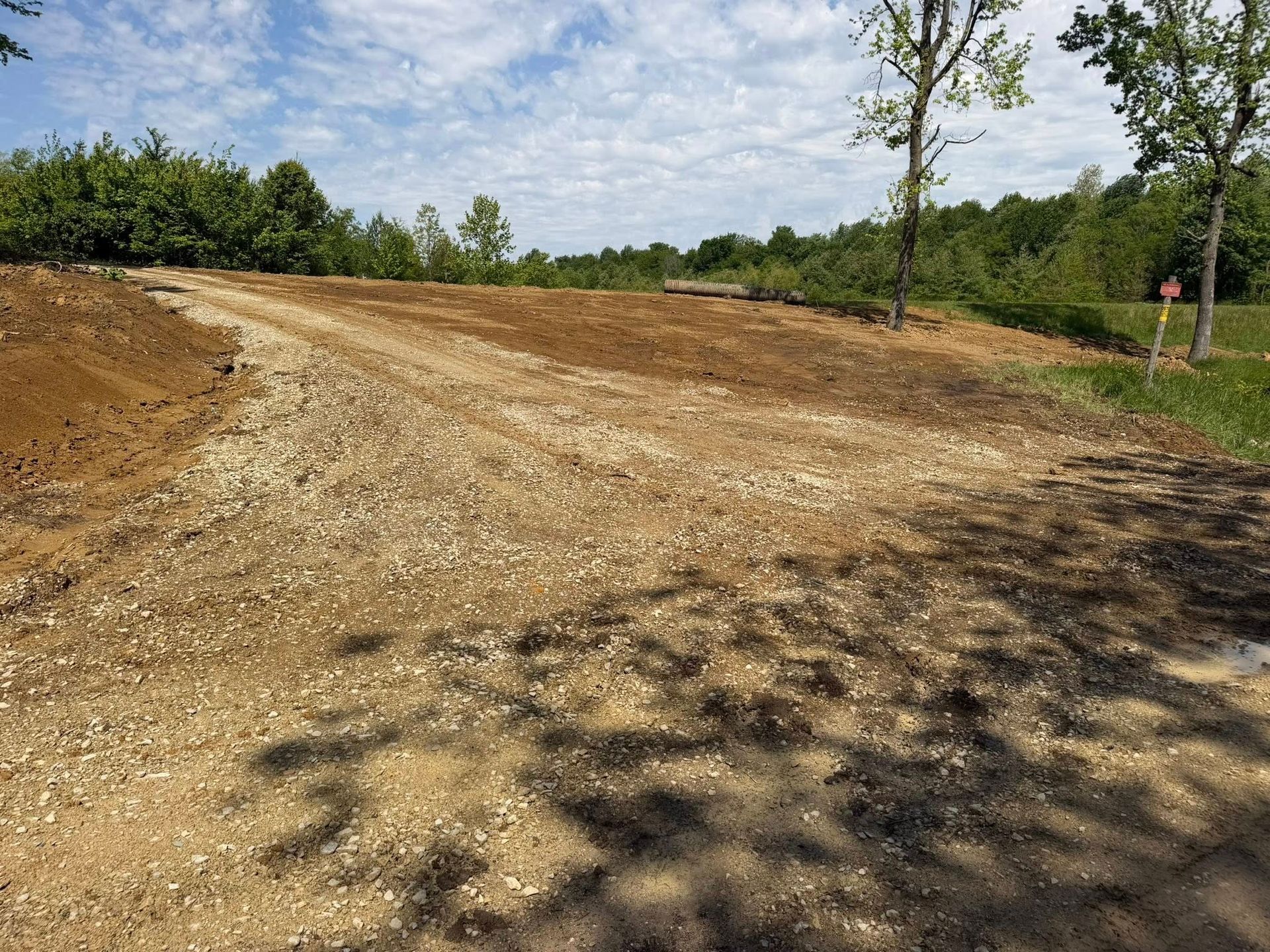 Dirt road construction site with graded brown earth, trees, and blue sky in the background