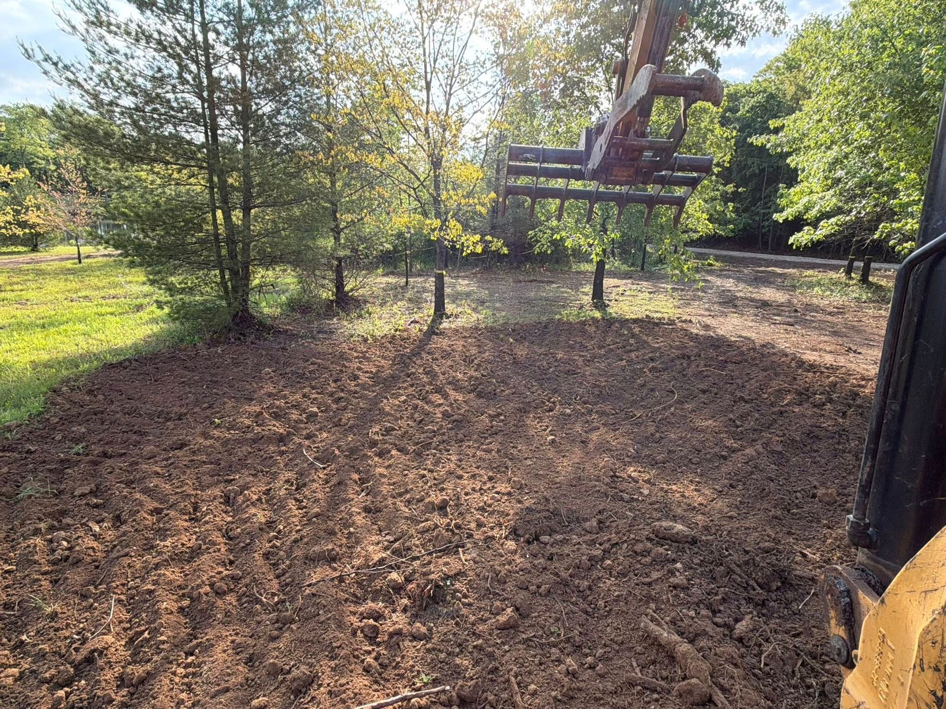 Tractor clearing a muddy dirt path in a wooded area on a sunny day