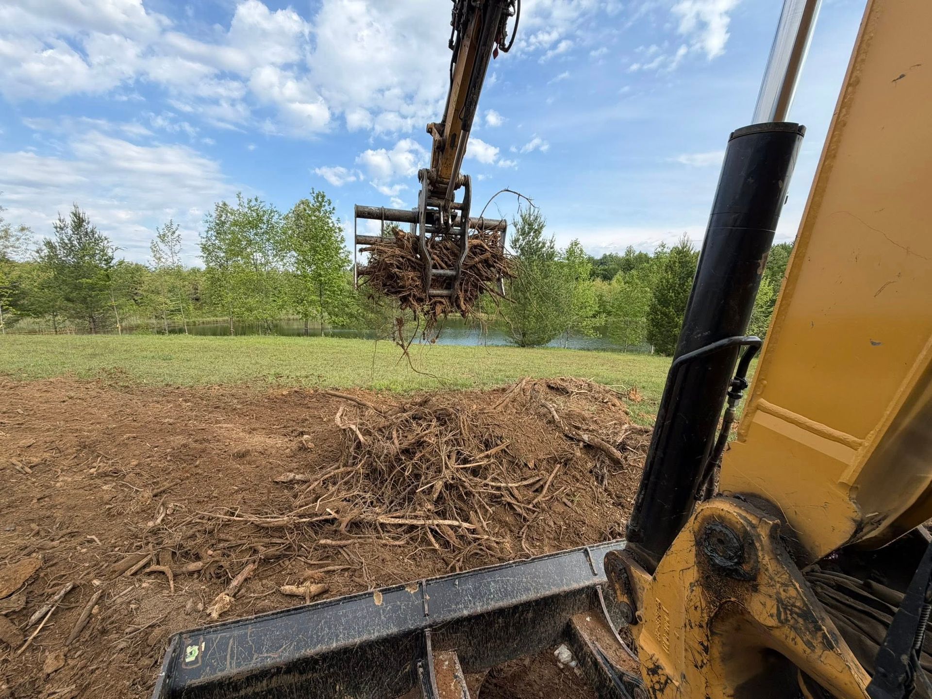 Excavator clearing brush in a grassy field under a blue sky