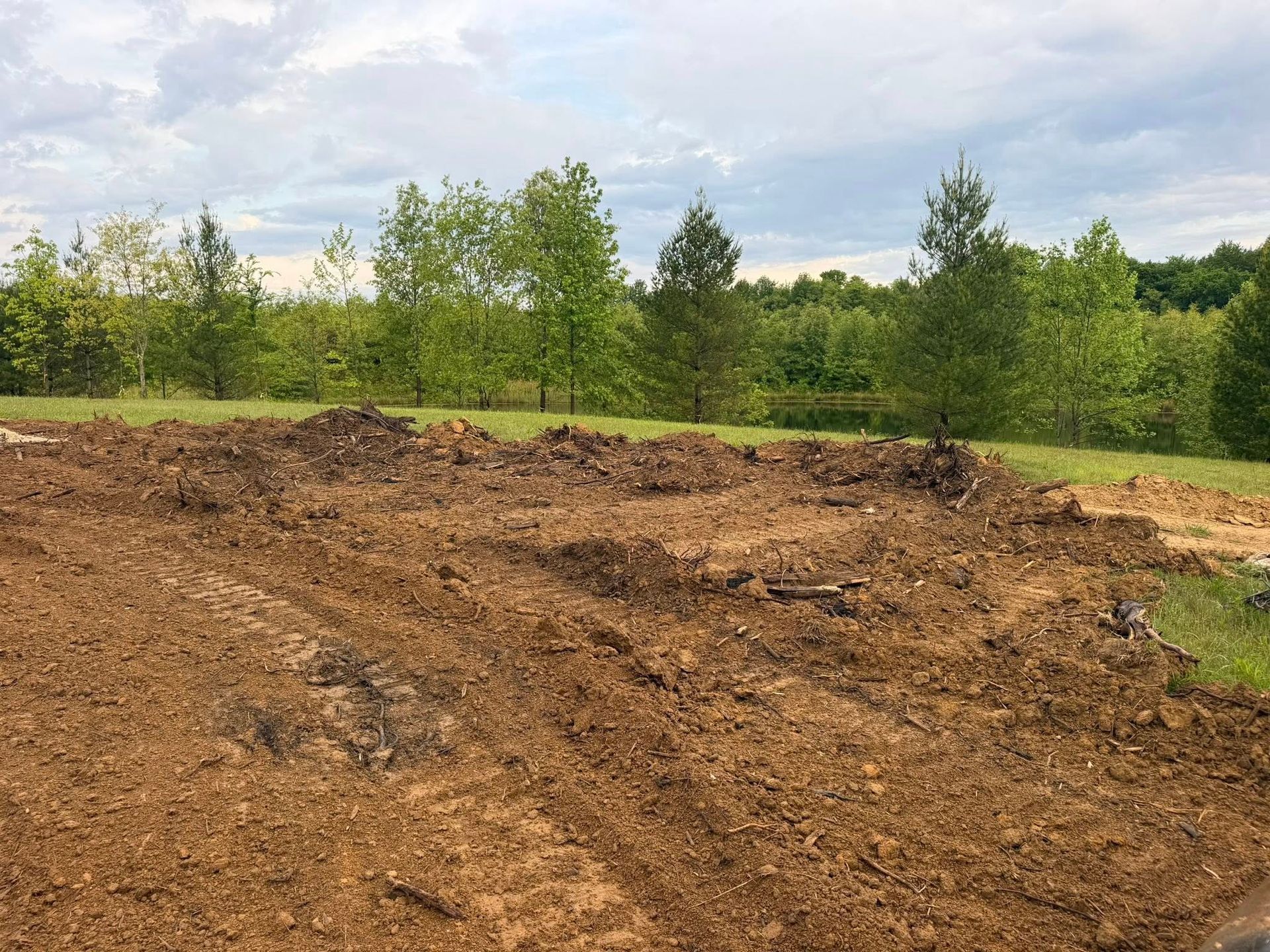 Freshly cleared brown dirt lot with green trees under a cloudy sky