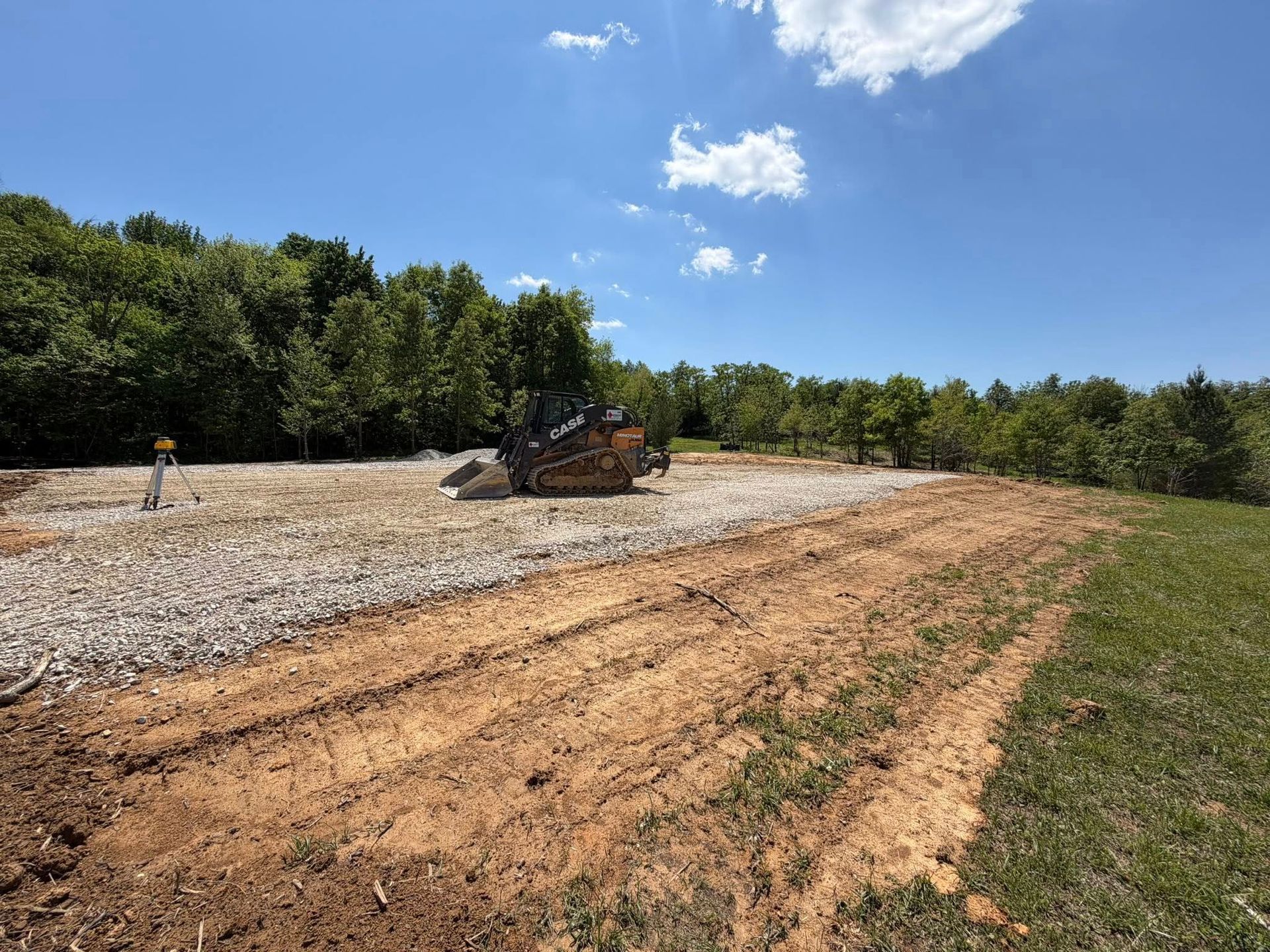 Bulldozer on a dirt clearing under a blue sky, with trees along the edge of the site
