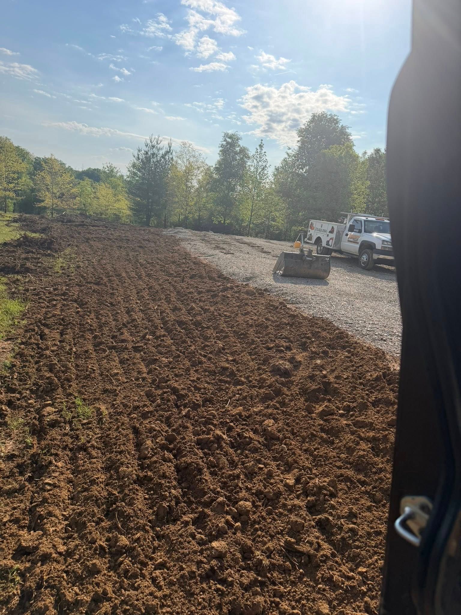 Fresh mulch pile beside a gravel road with a white truck under a sunny sky