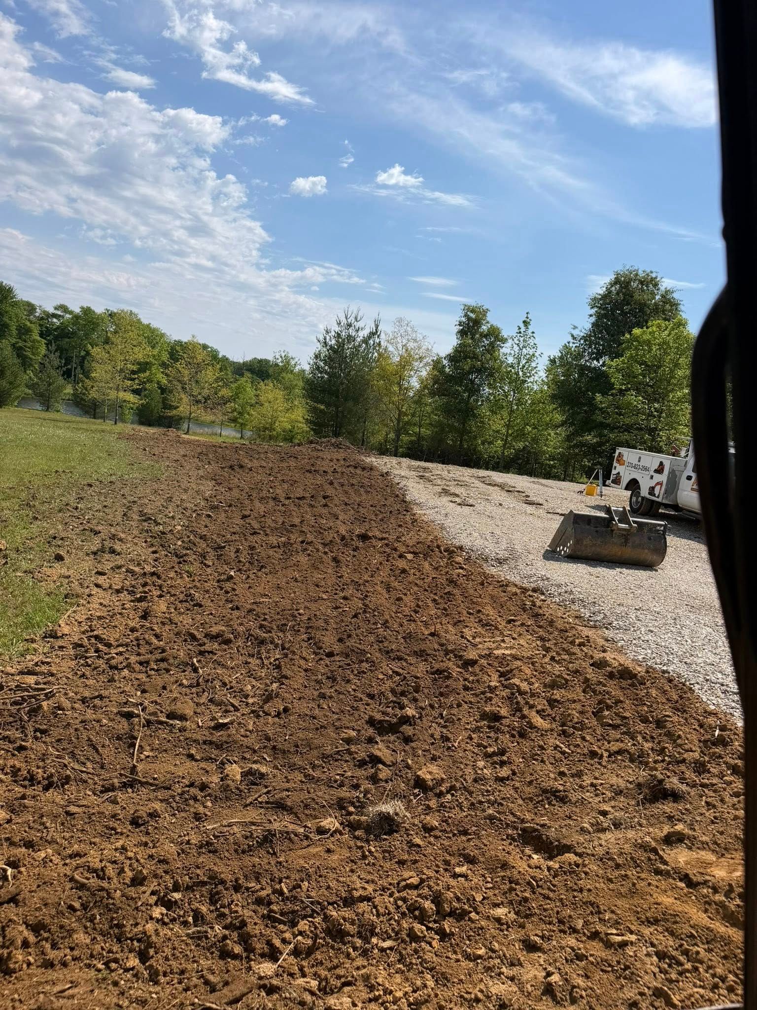 Freshly spread mulch or soil in a sunny landscaped yard with gravel edge and trees in the background