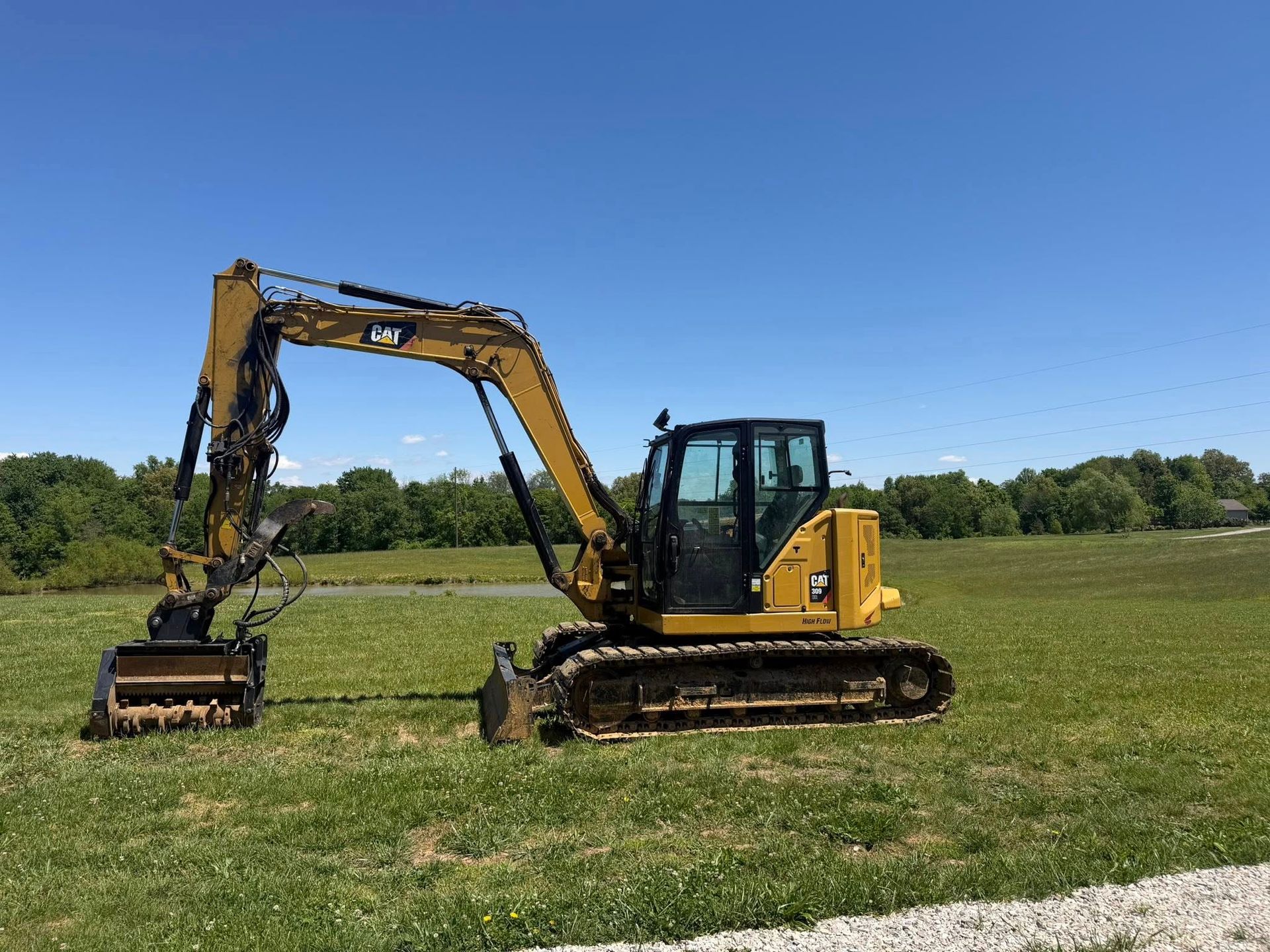 Yellow excavator on tracks in a grassy field under a clear blue sky