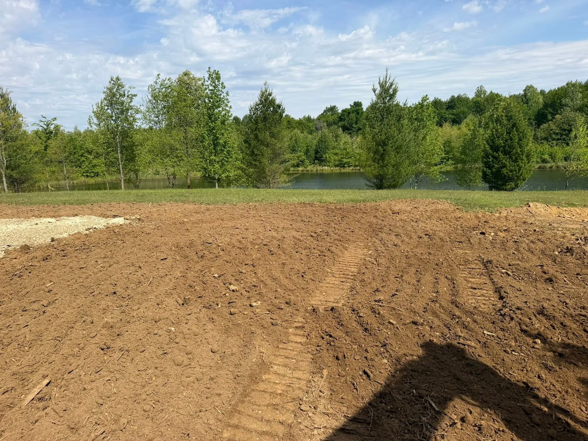Freshly graded dirt in the foreground with a green tree line and blue sky beyond