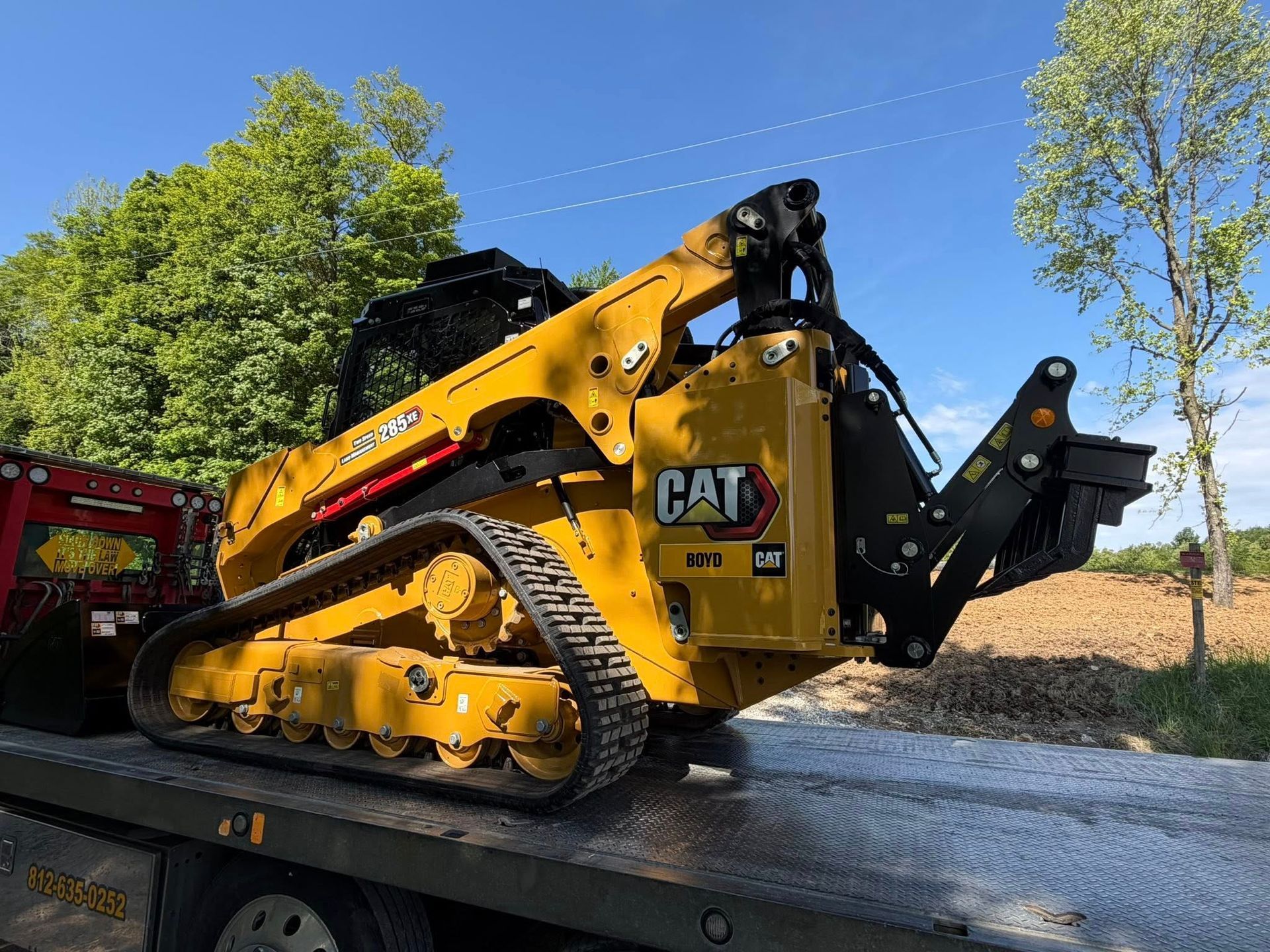 Yellow CAT compact track loader on a gravel road with trees and blue sky in the background