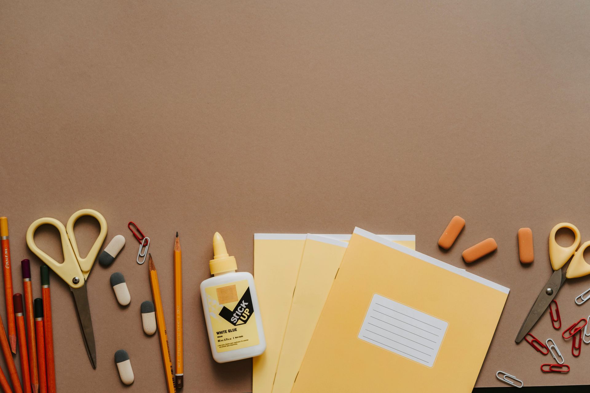 Foto vanFinch Logopediepraktijk, Schoolspullen uitgestald op een bruine ondergrond: potloden, lijm, schaar, gummen, papier.