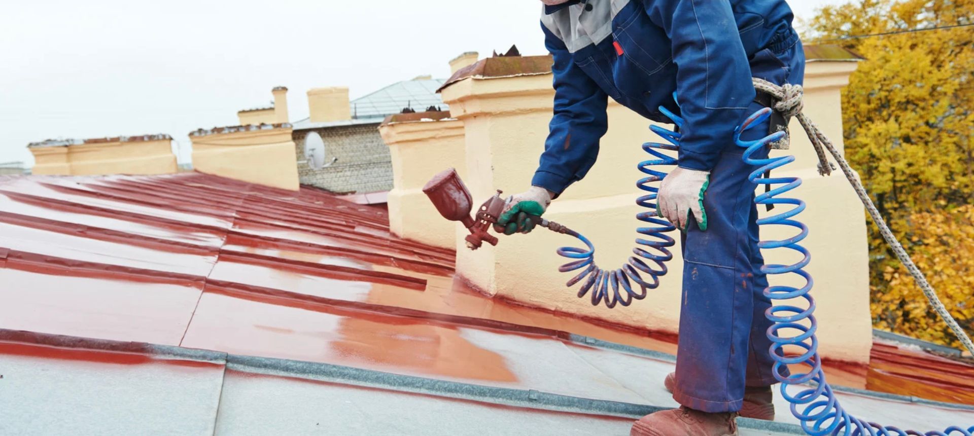 Roofer on a roof wearing a harness, hammering shingles. Gray shingles, bright green harness, blue sky.