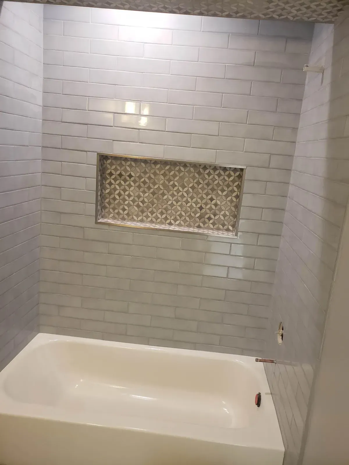 Bathroom with gray tiled walls, a built-in shelf with decorative tile, and a white bathtub.