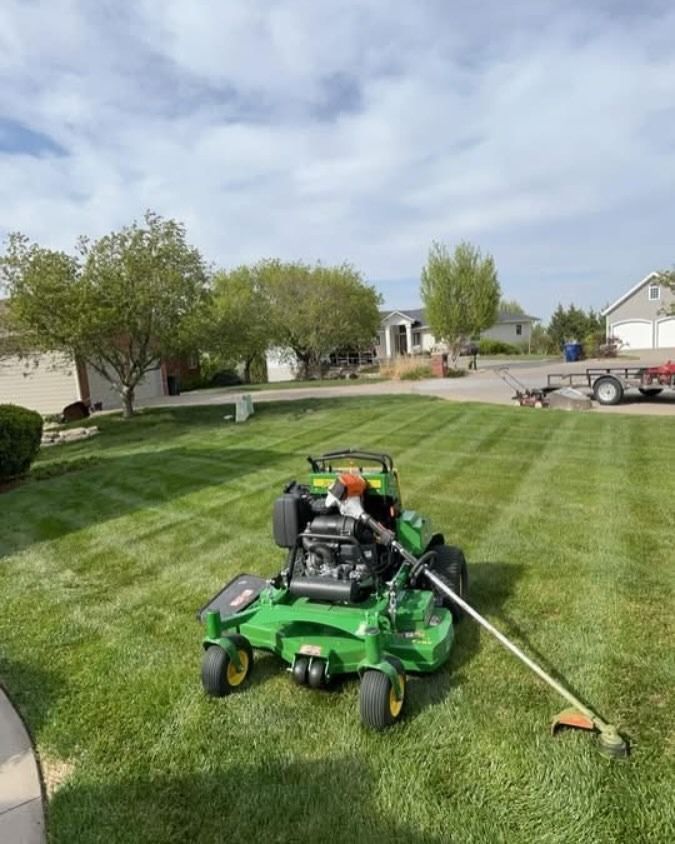 Green riding lawn mower and weed whacker on a freshly mowed lawn in a suburban neighborhood.