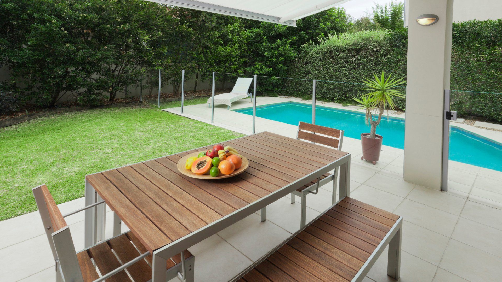 Nice backyard with a small pool surrounded by cedar hedges. There is a covered porch area with an eating area. The pool deck surrounding the pool is stamped concrete.