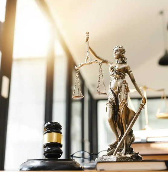 Law scale, gavel, and Lady Justice statue on a desk in a sunlit law office